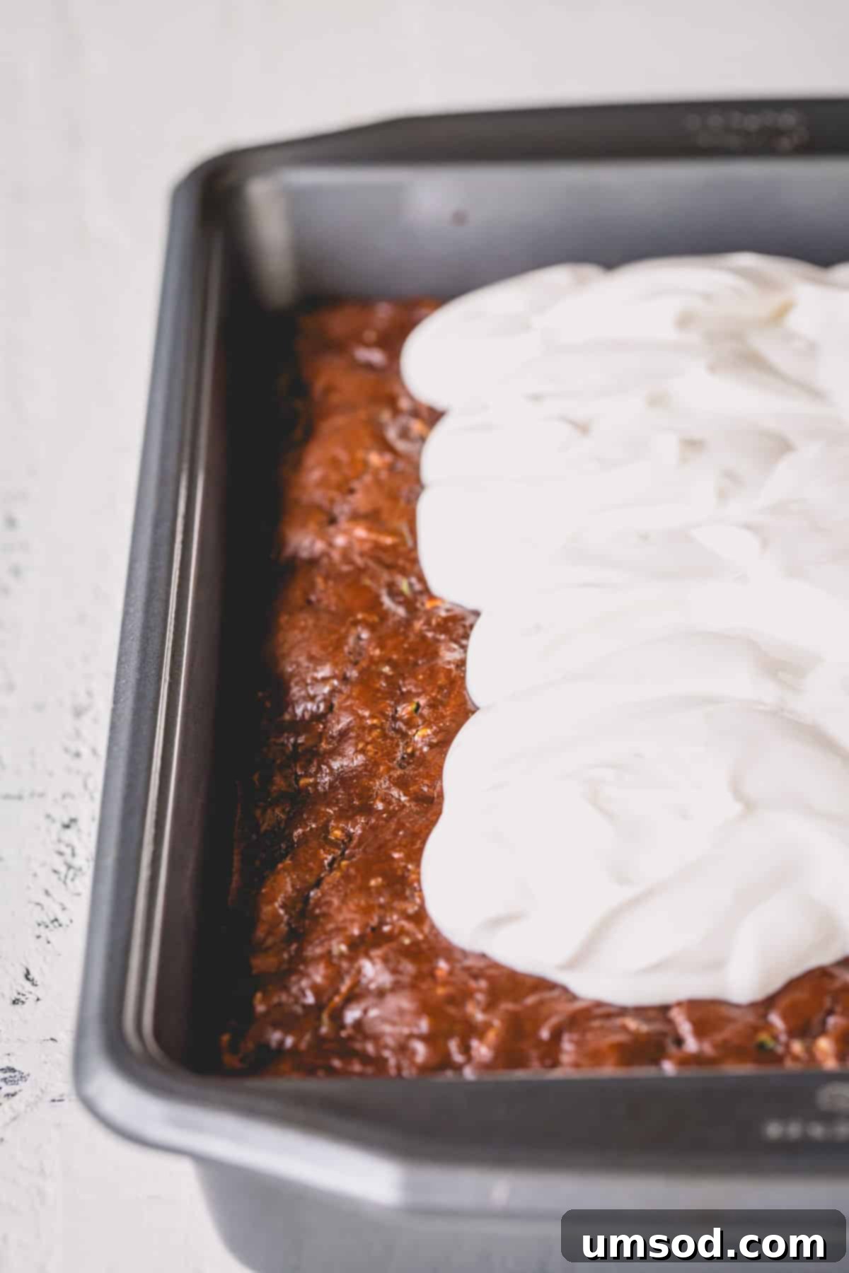 Fudgy Chocolate Zucchini Sheet Cake 8 A panoramic shot of the finished chocolate zucchini cake in a pan, partially frosted with dollops of sour cream frosting, ready for serving.