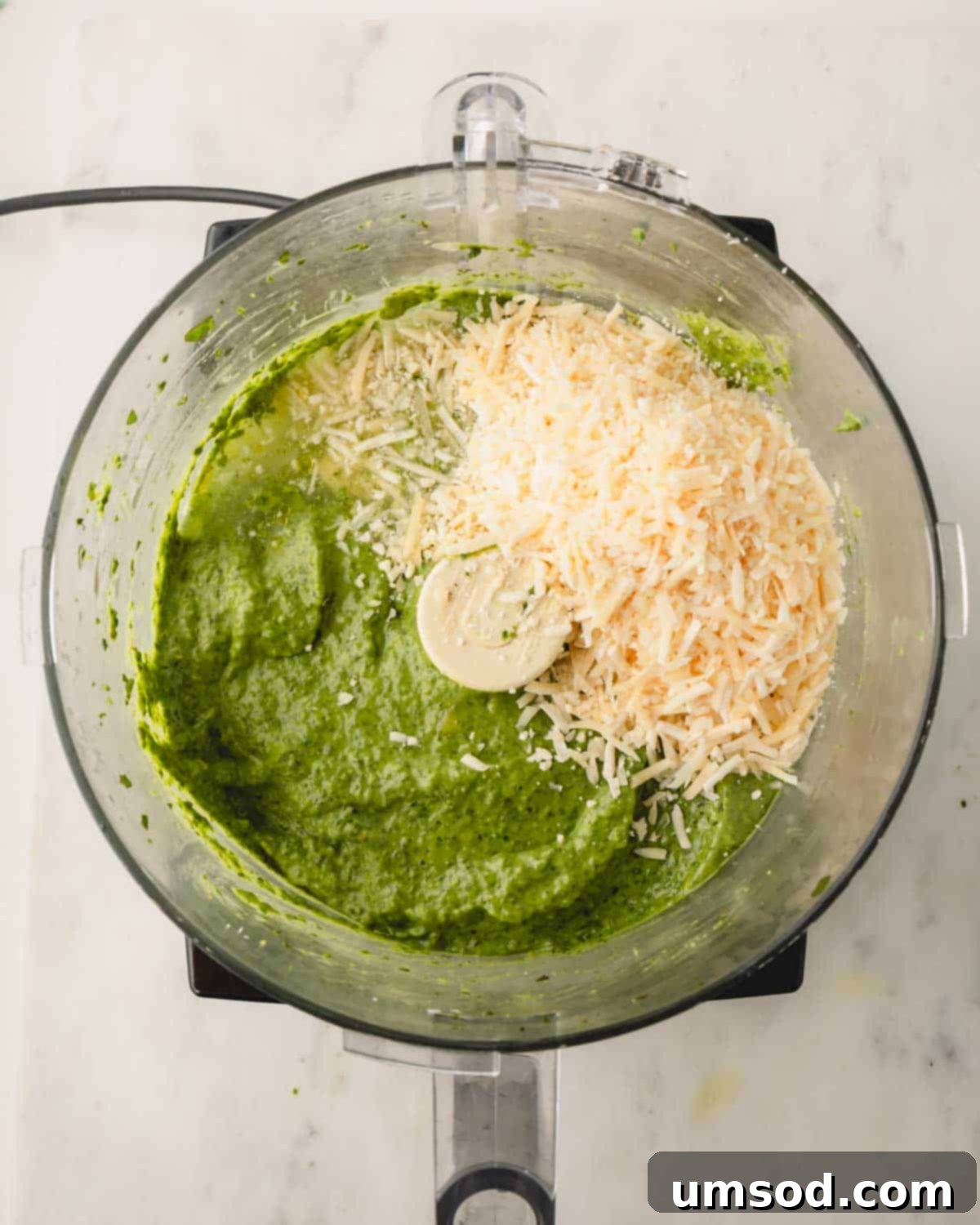 Big Batch Basil Pesto Recipe 12 Parmesan cheese added on top of the blended basil pesto in a food processor, ready for final processing.