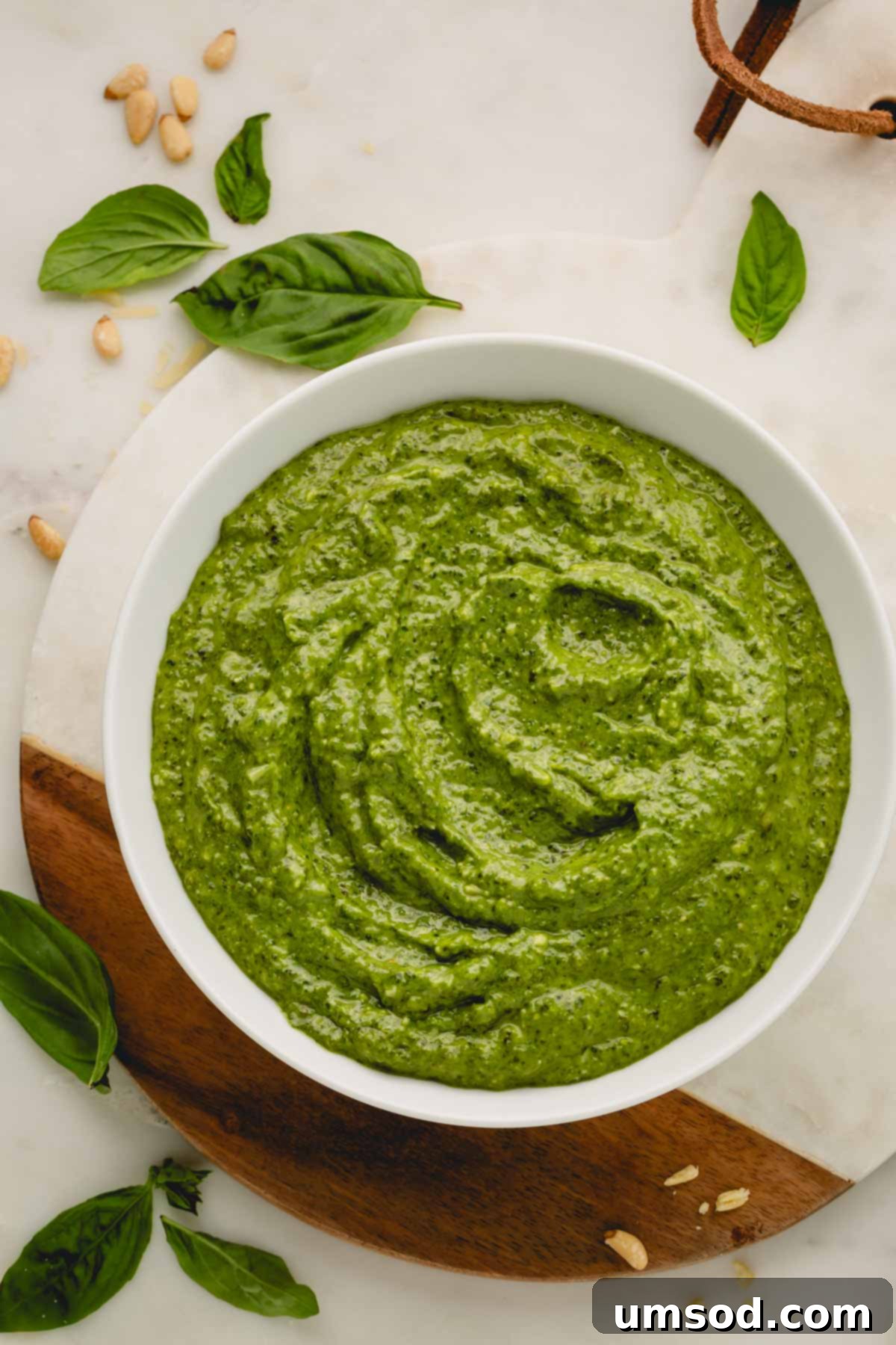 Big Batch Basil Pesto Recipe 14 A beautifully presented white bowl of large batch basil pesto on a serving platter, garnished with fresh basil leaves and toasted pine nuts.