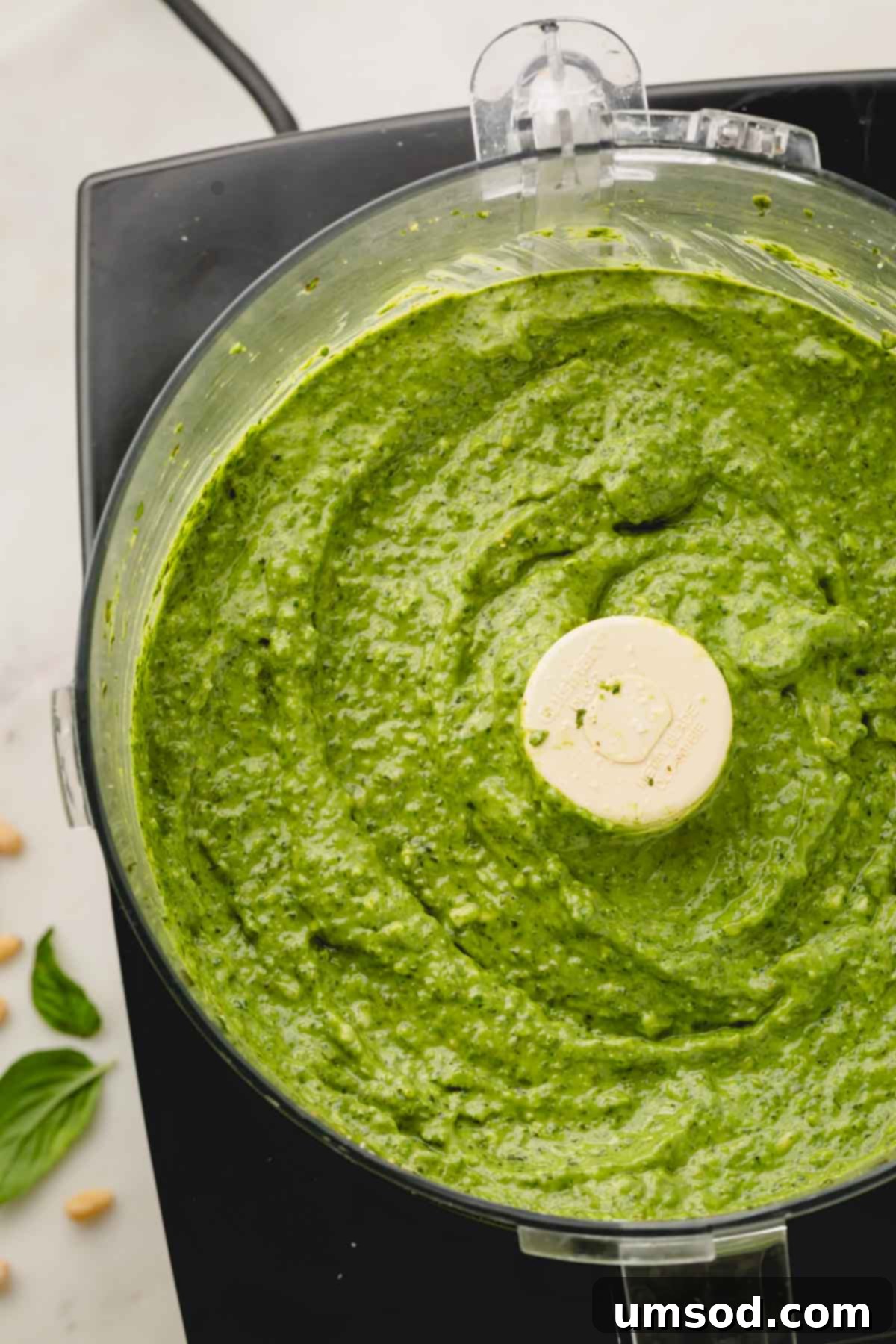 Big Batch Basil Pesto Recipe 3 Fresh basil pesto being processed in a food processor, showing its bright green color.