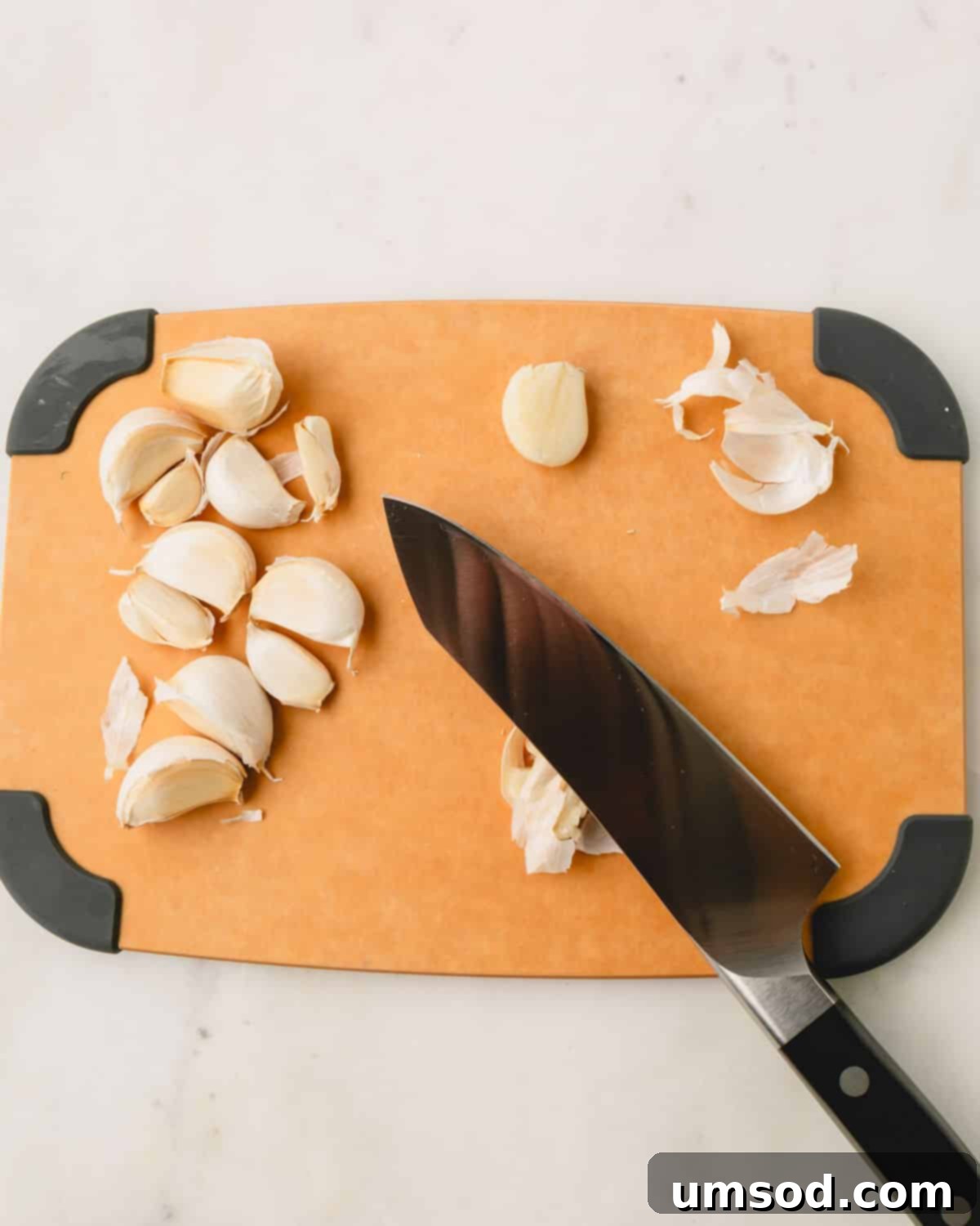 Big Batch Basil Pesto Recipe 8 A wooden cutting board displaying garlic cloves and a knife, ready for smashing and peeling.