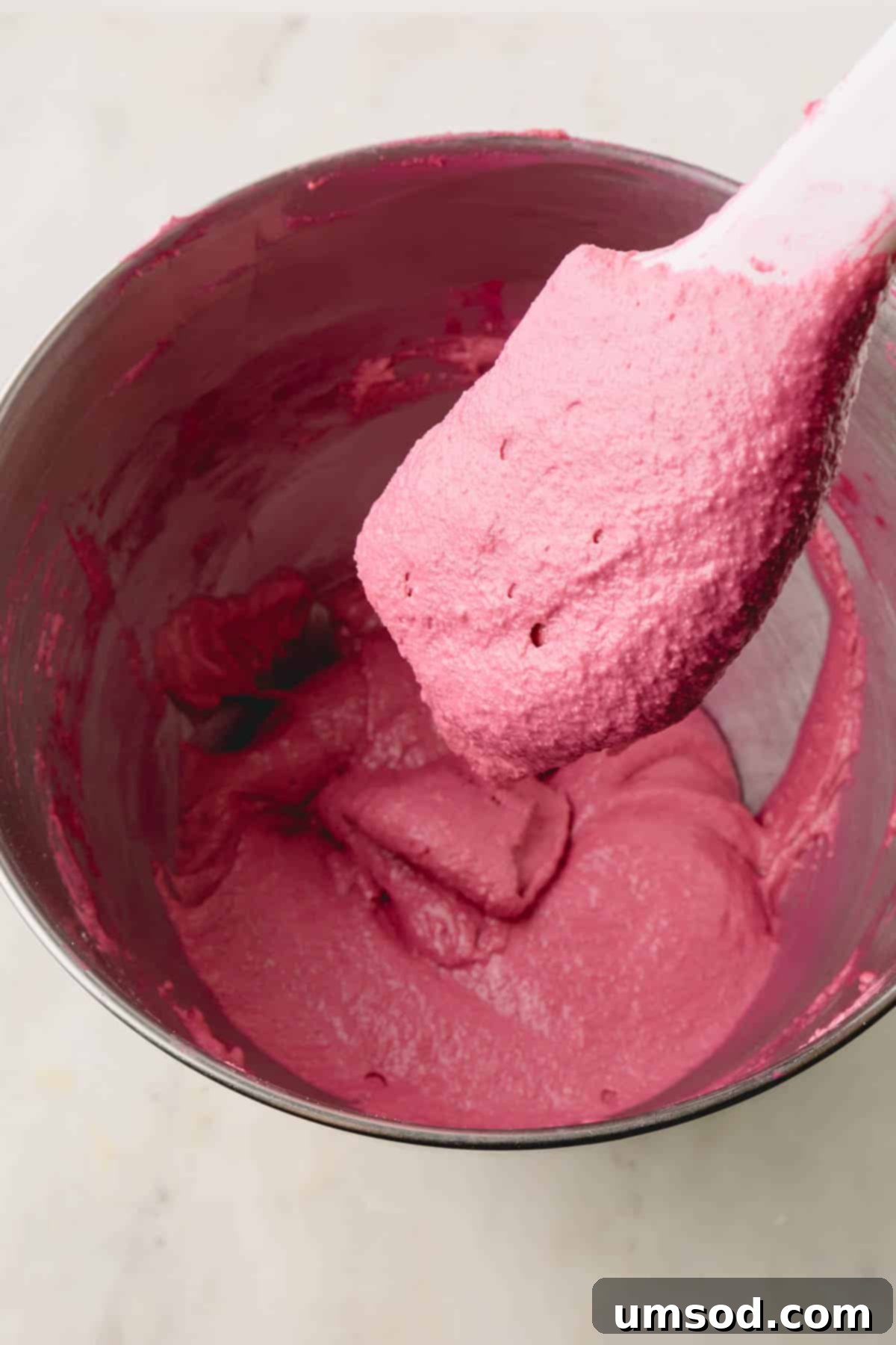 Cranberry Citrus Macarons 12 A spatula lifting a scoop of cranberry meringue batter, demonstrating the flowing ribbon consistency.