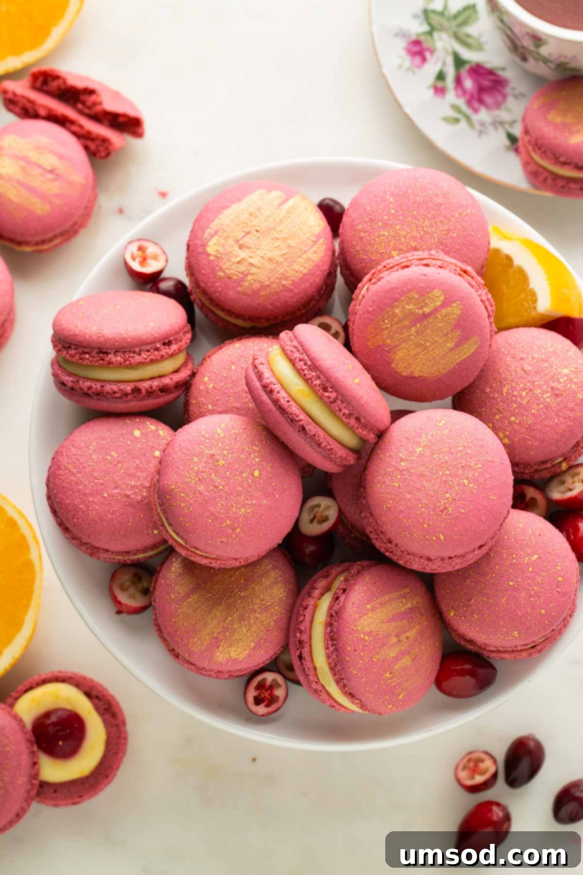 Cranberry Citrus Macarons 3 A tiered cake stand elegantly displaying cranberry orange macarons, lightly dusted with shimmering gold dust.