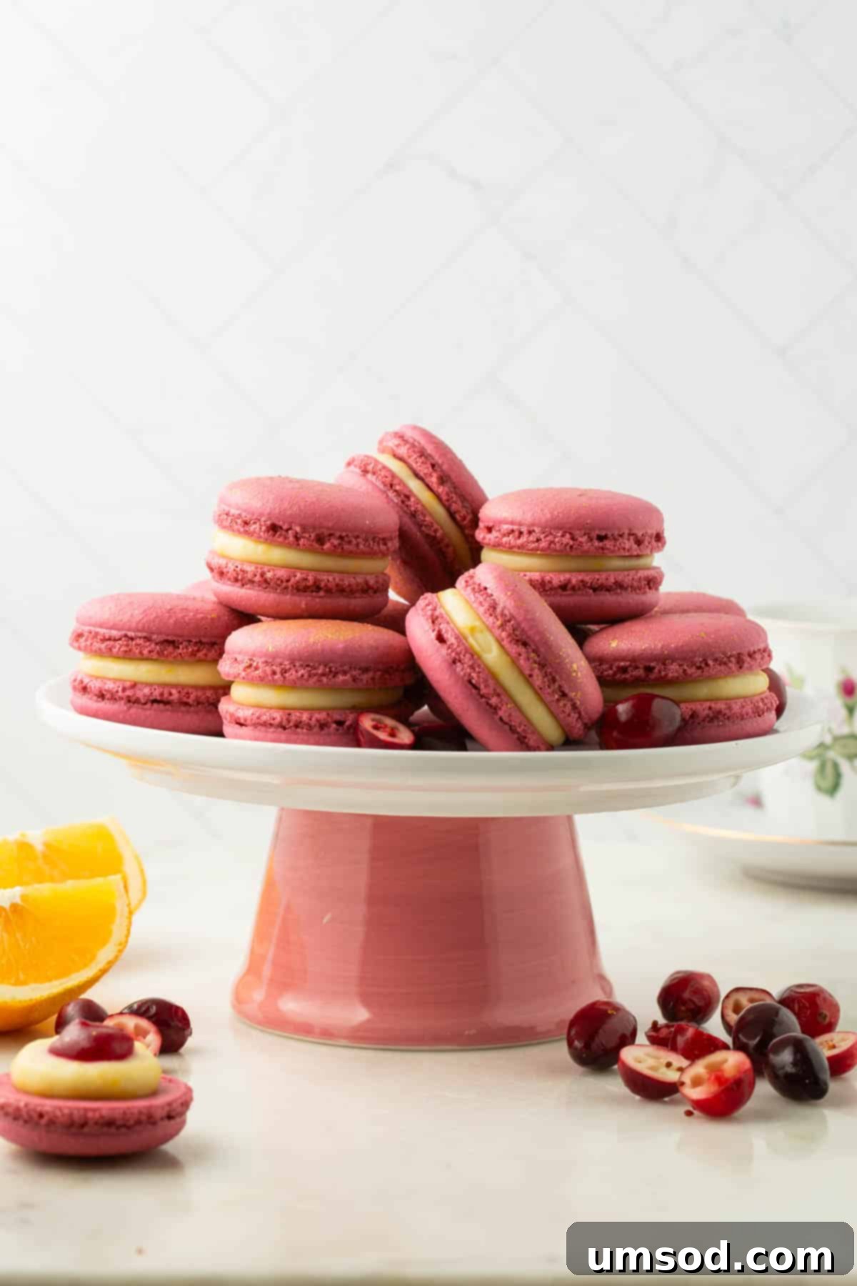 Cranberry Citrus Macarons 29 An elegant pink cake stand displaying a beautiful collection of orange cranberry macarons.